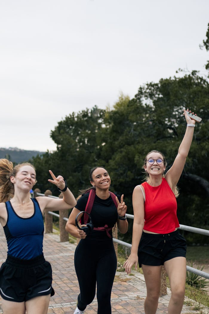 Three diverse women jogging outdoors, smiling and showing peace signs on a park path.