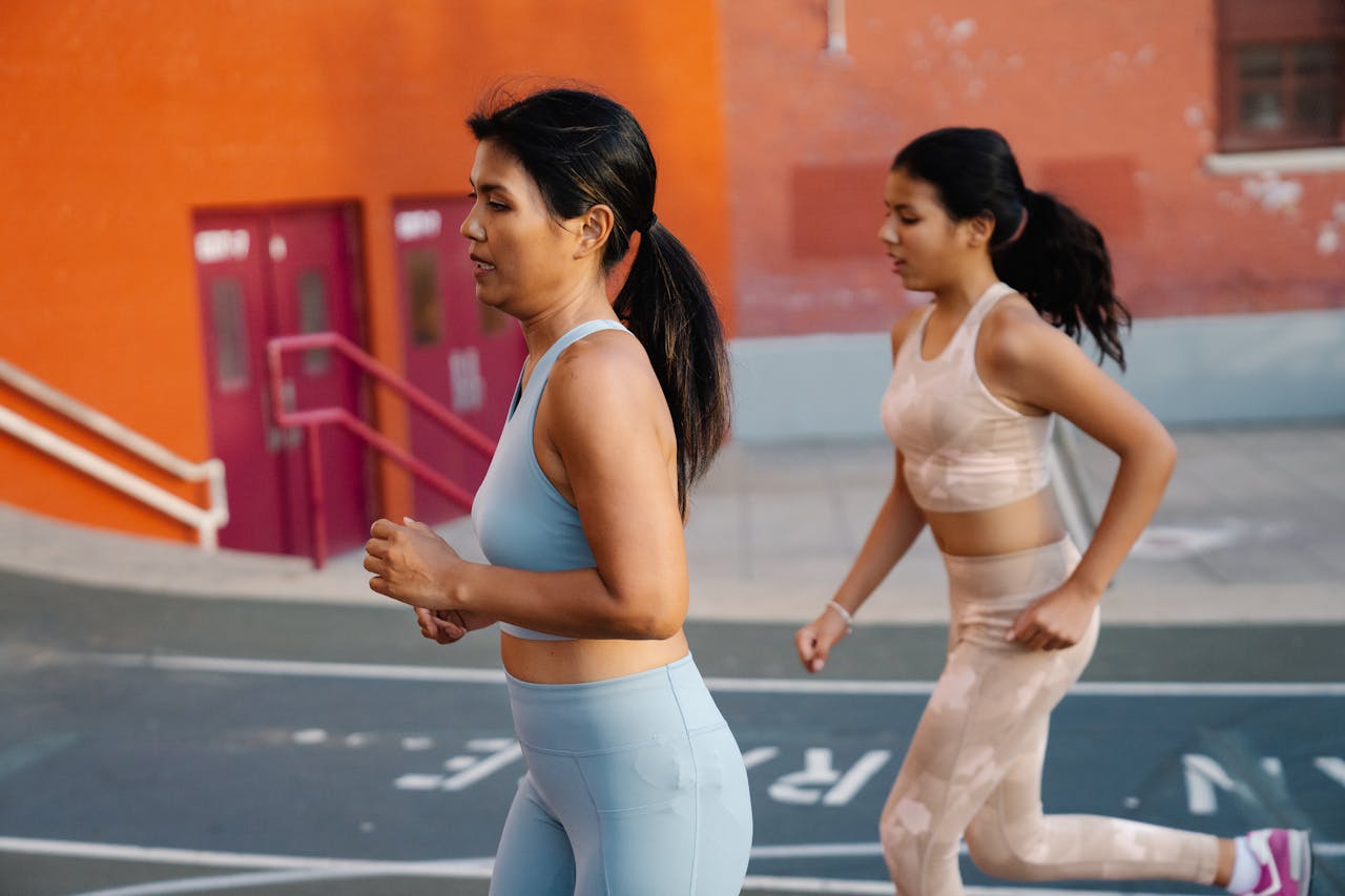 Two women in athletic gear jogging on a city pavement, promoting health and fitness.
