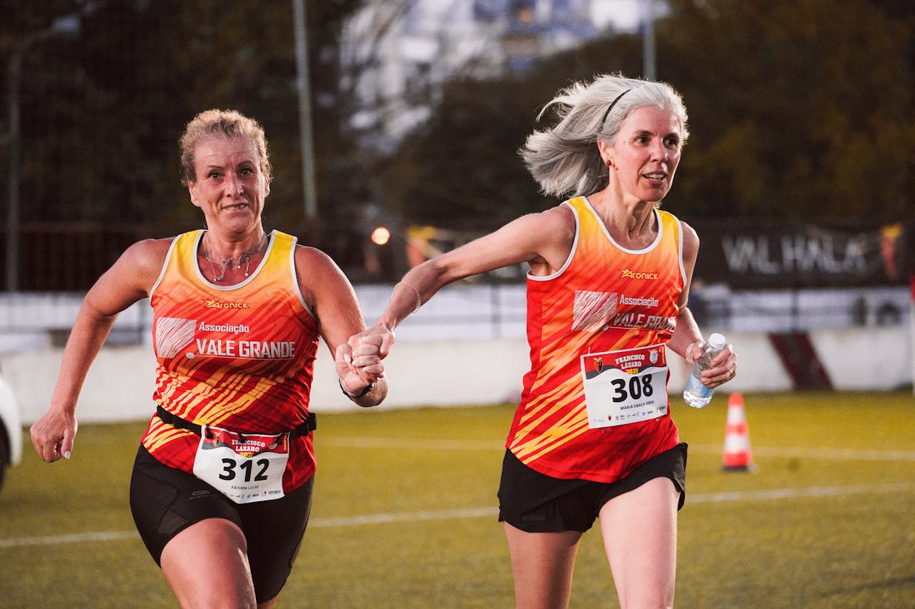Two senior women running hand in hand during a marathon event outdoors.